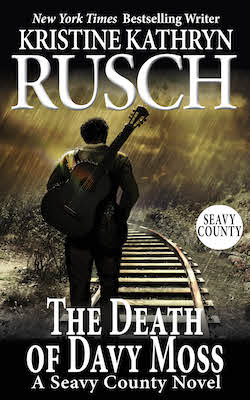 A man with a guitar walking along a railroad track in the rain.